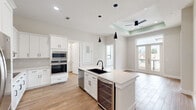 Located at 900 New Day Avenue in Montgomery, TX, this well-appointed 2-bedroom, 2-bathroom residence offers a thoughtfully designed single-level layout with modern finishes throughout. Wood-look tile flooring flows seamlessly across the entire home, lending warmth and visual continuity to every room.

The open-concept kitchen and living area serves as the heart of the home. The kitchen is outfitted with crisp white shaker cabinetry, a classic penny-tile backsplash, light quartz countertops, and a central island featuring a matte black undermount sink with pendant lighting above. Stainless steel appliances — including a French door refrigerator, double wall oven, built-in microwave, dishwasher, and a wine refrigerator — complete this chef-ready space. A dedicated laundry area with a stacked washer and dryer is conveniently accessible off the kitchen.

The living area benefits from a tray ceiling and French doors that open to a private balcony, filling the space with natural light and outdoor views. Both bedrooms are bright and airy, each featuring recessed lighting and black-framed windows. The primary bedroom includes a spacious walk-in closet with built-in shelving. The bathrooms are elegantly finished, with one showcasing a frameless glass shower enclosure adorned with floor-to-ceiling marble-look tile and matte black hardware.