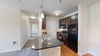 Located at 4000 Mullan Rd in Missoula, Montana, this two-bedroom, one-bathroom unit offers a well-organized, single-level layout designed for comfortable everyday living. The open-concept kitchen and living area serves as the heart of the home, where a peninsula island with dark granite-style countertops and pendant lighting creates a natural gathering space. Rich, dark-stained cabinetry lines the kitchen walls alongside black appliances, including a refrigerator, range, and built-in microwave, all set atop warm hardwood-style flooring. The living room is bright and inviting, with plush carpeting and a sliding glass door that opens to a private balcony overlooking lush greenery. Both bedrooms are carpeted and feature natural light from windows with exterior views. The primary bedroom benefits from a walk-in closet with built-in wire shelving, providing generous storage. The second bedroom is a quiet, well-proportioned space with clean, neutral walls. The bathroom includes a full tub-shower combination with a curved curtain rod and a safety grab bar. A dedicated closet and additional storage options complete this thoughtfully designed, move-in-ready home in the heart of Missoula.