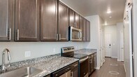 This thoughtfully designed one-bedroom, one-bathroom unit maximizes every square foot across a single floor. The open-concept kitchen and living area serves as the heart of the space, featuring rich dark espresso cabinetry with sleek silver hardware, speckled granite countertops, and a full suite of stainless steel appliances including a refrigerator, range, over-the-range microwave, and dishwasher. Recessed lighting and a window with natural light brighten the living area, which flows seamlessly from the kitchen along warm wood-style flooring that extends throughout the unit. A hallway connects the main living space to the private areas of the home. The bedroom is a cozy, well-proportioned retreat with neutral-toned walls, wood-style flooring, and a ceiling fan. The bathroom continues the consistent design language with matching dark cabinetry, granite countertop vanity, an undermount sink, a wall-mounted medicine cabinet, a large mirror, and a tiled shower-tub combination. Clean white panel doors and crisp white baseboards lend a polished, cohesive finish to the entire unit. The overall aesthetic is modern and functional, with consistent finishes creating a unified, move-in-ready living environment.