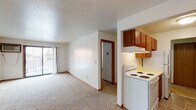 Located at 2530 14th St S in Fargo, North Dakota, this single-floor unit offers a functional and straightforward layout across several distinct living areas. The living room is generously sized, featuring wall-to-wall carpeting, a ceiling fan with light fixture, wood-paneled wainscoting along one wall, a textured ceiling, and a wall-mounted air conditioning unit. A sliding glass door floods the space with natural light and provides access to a private balcony with views of the surrounding neighborhood.

The galley-style kitchen is positioned adjacent to the living area and is equipped with warm-toned wood cabinetry on both sides, a yellow laminate countertop with an integrated sink, a white electric range with overhead ventilation, a refrigerator, and tile flooring. Lower wood wainscoting continues into this space, maintaining a consistent design throughout.

The unit includes two bedrooms, each carpeted and finished with white walls, wood-trimmed bi-fold closet doors, and adequate built-in closet storage with hanging rods. The bathroom features tile flooring, a wood-trimmed vanity with a mirror above, a toilet, and a full tub-shower combination. The textured ceilings and warm wood trim details are consistent throughout the unit, contributing to a cohesive, classic interior character.