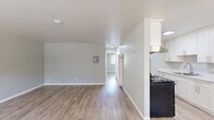 Located at 2211 Redwood St in Vallejo, CA, this 2-bedroom, 1-bathroom unit offers a clean, modern interior spread across a single floor. Light wood-look plank flooring flows consistently throughout the space, complementing the soft gray walls and crisp white trim found in every room.

The living room is a welcoming, open area anchored by large windows fitted with horizontal blinds, allowing ample natural light to fill the room. Views of palm trees and the surrounding neighborhood are visible from the front-facing windows, adding a pleasant outdoor connection. The living area includes a utility panel and provides a clear sightline to the rest of the unit.

The galley-style kitchen is efficiently designed with white shaker cabinetry lining both walls, a light quartz countertop, a stainless steel sink, and black appliances including a range and refrigerator. An overhead range hood and generous upper cabinet storage make this kitchen highly functional.

Both bedrooms are well-proportioned and filled with natural light from exterior-facing windows. Each room features a sliding double-door closet, offering substantial storage. The primary bedroom is notably spacious and includes room for a full furniture arrangement.

The bathroom is finished with a white tiled tub-shower combination and gold-toned fixtures, maintaining a clean, classic aesthetic throughout.