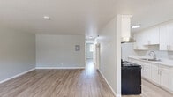 Located at 2211 Redwood St in Vallejo, CA, this 2-bedroom, 1-bathroom unit offers a clean, modern interior spread across a single floor. Light wood-look plank flooring flows consistently throughout the space, complementing the soft gray walls and crisp white trim found in every room.

The living room is a welcoming, open area anchored by large windows fitted with horizontal blinds, allowing ample natural light to fill the room. Views of palm trees and the surrounding neighborhood are visible from the front-facing windows, adding a pleasant outdoor connection. The living area includes a utility panel and provides a clear sightline to the rest of the unit.

The galley-style kitchen is efficiently designed with white shaker cabinetry lining both walls, a light quartz countertop, a stainless steel sink, and black appliances including a range and refrigerator. An overhead range hood and generous upper cabinet storage make this kitchen highly functional.

Both bedrooms are well-proportioned and filled with natural light from exterior-facing windows. Each room features a sliding double-door closet, offering substantial storage. The primary bedroom is notably spacious and includes room for a full furniture arrangement.

The bathroom is finished with a white tiled tub-shower combination and gold-toned fixtures, maintaining a clean, classic aesthetic throughout.