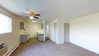 This single-floor unit at 2650 Ingalls offers an open-concept layout that seamlessly connects the living area and kitchen. The carpeted living space is generously sized, providing a comfortable and versatile area for everyday use. Two closets with bifold doors are conveniently positioned along the living area wall, offering substantial built-in storage.

The kitchen flows directly from the living space and features hardwood-style flooring, gray cabinetry, a white electric range, a refrigerator, and a sink with an under-cabinet window above. A peninsula counter serves as a natural dividing element between the kitchen and living area, adding functional workspace and a subtle sense of separation without closing off the open feel.

A ceiling fan with a light fixture is centrally mounted in the living area, contributing to air circulation and ambient lighting. The textured ceilings are consistent throughout the space. A hallway extends beyond the kitchen, suggesting additional rooms toward the rear of the unit. The overall palette is neutral, with white walls and light tones that create a bright, clean atmosphere throughout.