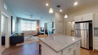 This single-story residence is designed with a contemporary, open-concept layout that seamlessly connects the kitchen and living areas. The kitchen is well-appointed with white shaker-style cabinetry, granite countertops, a large central island with bar seating, stainless steel appliances including a range, microwave, dishwasher, and refrigerator, and a herringbone-patterned tile backsplash. Wood-look flooring extends through the kitchen and living spaces, while pendant lighting above the island adds a polished touch.

The living area is bright and inviting, benefiting from large windows dressed with horizontal blinds and sheer curtains that allow generous natural light. A ceiling fan and recessed lighting provide additional illumination. Access to an outdoor area is available through a windowed door in the living room.

The residence includes multiple bedrooms, each carpeted and featuring windows with blinds and curtains. Each bedroom is accompanied by a private bathroom with granite-topped vanities and tile flooring, as well as a dedicated walk-in closet with built-in shelving. The overall color palette is neutral and consistent throughout, contributing to a clean, cohesive aesthetic.