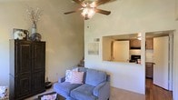 This two-story residence makes a strong first impression with its dramatically vaulted ceilings in the main living area, which rise well above standard height and are complemented by a ceiling fan with a decorative light fixture. The generous vertical space lends an airy, open quality to the living room, which is finished with neutral-toned walls and carpeted flooring, creating a warm and comfortable atmosphere. A staircase along one wall provides access to the second floor, tucked naturally into the layout without disrupting the flow of the main living space. A standout architectural feature is the pass-through window opening that connects the living room to the kitchen above, offering both visual connectivity between the two spaces and a sense of openness throughout. The kitchen, visible through this opening, features wood-toned cabinetry and standard appliances, including a range. The overall design balances functionality with an inviting aesthetic, making good use of vertical space to enhance the sense of scale throughout the home.