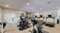 Located at Greystone at Whittlesey Blvd in Columbus, Georgia, this fitness center offers a generously sized, single-floor exercise space designed to support a full range of workout routines. The room features neutral-toned walls, carpeted flooring with protective rubber mats beneath equipment, and recessed lighting throughout, creating a clean and functional environment.

The cardio section is well-appointed with multiple True-brand treadmills, upright and recumbent stationary bikes, and elliptical machines, providing ample options for aerobic training. The strength training area includes a multi-station cable and weight machine system, a dedicated dumbbell rack, and a free weight station with a barbell and weight plates, catering to users of varying fitness levels.

Large wall-to-wall mirrors span one side of the room, enhancing the sense of space and allowing users to monitor their form during workouts. Fitness reference charts and motivational posters are displayed on the walls, adding an informative and encouraging atmosphere. Natural light enters through a set of French doors along one wall, connecting the interior to the outdoors. An exit door provides convenient access. The overall design is practical and welcoming, making this fitness center a comprehensive amenity for residents seeking an accessible and well-maintained place to exercise.