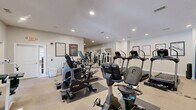 Located at Greystone at Whittlesey Blvd in Columbus, Georgia, this fitness center offers a generously sized, single-floor exercise space designed to support a full range of workout routines. The room features neutral-toned walls, carpeted flooring with protective rubber mats beneath equipment, and recessed lighting throughout, creating a clean and functional environment.

The cardio section is well-appointed with multiple True-brand treadmills, upright and recumbent stationary bikes, and elliptical machines, providing ample options for aerobic training. The strength training area includes a multi-station cable and weight machine system, a dedicated dumbbell rack, and a free weight station with a barbell and weight plates, catering to users of varying fitness levels.

Large wall-to-wall mirrors span one side of the room, enhancing the sense of space and allowing users to monitor their form during workouts. Fitness reference charts and motivational posters are displayed on the walls, adding an informative and encouraging atmosphere. Natural light enters through a set of French doors along one wall, connecting the interior to the outdoors. An exit door provides convenient access. The overall design is practical and welcoming, making this fitness center a comprehensive amenity for residents seeking an accessible and well-maintained place to exercise.