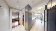 This efficiently designed 2-bedroom, 1-bathroom residence makes excellent use of its single-floor layout, offering a well-organized living space with distinct rooms for every function. The kitchen is a standout feature, showcasing sleek gray cabinetry, stainless steel appliances including a range, microwave, and refrigerator, and a striking textured accent wall with a crocodile-pattern finish. Light tile flooring runs through the kitchen and hallway, creating a clean, bright corridor that connects the main living areas. The living room is an inviting retreat, featuring warm hardwood floors, plantation shutters that filter natural light, a wall-mounted mini-split unit, and a cozy seating arrangement centered around a round wooden coffee table. Both bedrooms continue the hardwood flooring theme and are served by radiator heating. The primary bedroom accommodates a workspace alongside sleeping quarters, while the second bedroom offers a compact and functional layout with a window and wall sconce lighting. The bathroom is finished with white tile flooring, a pedestal sink, a large mirror with vanity lighting, and a tiled shower enclosure. A tall built-in pantry cabinet in the hallway adds valuable storage to this thoughtfully arranged home.