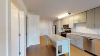 This single-floor residence presents a clean, contemporary design throughout its well-organized layout. The kitchen serves as a central highlight, outfitted with gray shaker-style cabinetry extending to the ceiling for generous storage. Granite-style countertops run along the perimeter, complemented by a full suite of stainless steel appliances, including an electric range, over-the-range microwave, refrigerator, and dishwasher. A mobile kitchen island with a matching granite top adds flexible prep and dining space. Wood-look flooring anchors the kitchen and extends into the adjoining open entry area, lending warmth and continuity.

The bedroom is a comfortable, well-proportioned room finished with neutral carpet and crisp white walls. A reach-in closet with a rod provides practical storage, and a frosted-glass interior door allows soft light to filter through. The bathroom features light wood-look tile flooring, a full soaking tub, and a tiled surround accented with a decorative mosaic border band. The vanity offers additional storage. Overall, the unit maintains a bright, neutral palette throughout, creating a cohesive and functional living environment.