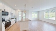 Located at 1 Hatcher Drive in Stockbridge, GA, this well-appointed 3-bedroom, 2-bathroom single-story home offers a thoughtfully designed layout with modern finishes throughout. The open-concept kitchen and living area serves as the heart of the home, featuring light hardwood-style flooring, recessed lighting, and abundant natural light from a glass door that opens to the outdoors. The kitchen is equipped with stainless steel appliances — including a refrigerator, range, microwave, and dishwasher — complemented by crisp white shaker cabinetry with matte black hardware, granite countertops, a herringbone tile backsplash, and a central island with pendant lighting above. The living area provides a clean, open canvas with neutral walls and smooth ceilings. The bedrooms are finished with plush carpeting and ceiling fans, and each is served by natural light through large windows. The primary bedroom includes a generously sized walk-in closet outfitted with wire shelving systems for organized storage. A second walk-in closet is also present. The bathrooms feature light wood-look flooring, white vanities with granite countertops, and a tiled shower. Clean lines, a neutral palette, and quality finishes define the overall aesthetic of this move-in-ready home.