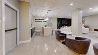 Located at 406 S Boulder Ave in downtown Tulsa, Oklahoma, this thoughtfully designed amenity lounge at the Beacon Building offers a dynamic and inviting communal environment spread across a single, open floor. The polished terrazzo flooring runs throughout the space, lending a sleek, cohesive foundation that reflects the recessed lighting overhead.

Upon entry, guests are welcomed by a vibrant neon "Coffee Bar Open" sign illuminating a dark-cabineted service counter, setting a lively yet stylish tone. This area transitions seamlessly into a central island workspace with pendant globe lighting above, ideal for casual gatherings or impromptu meetings.

The lounge zone features plush, curved velvet seating arrangements in deep charcoal tones paired with round white tables, perfect for socializing. A dedicated games area centers around a full-size billiards table, dramatically lit by two oversized gold pendant fixtures, with abstract wall art adding an artistic touch.

At the far end, a generous sectional sofa faces a striking wood-slat accent wall housing a wall-mounted television and a linear electric fireplace, creating a warm, theater-like retreat. A "Beacon Building" wall installation serves as a signature branding element throughout, tying the space to its historic downtown identity. The overall ambiance is modern, welcoming, and richly appointed.