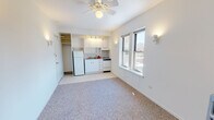 Located on N Winthrop Ave in Chicago's Edgewater neighborhood (60660), this single-floor studio offers a thoughtfully arranged open layout that combines living and kitchen functions efficiently. The main living area features neutral carpet flooring, crisp white walls, and a ceiling fan with integrated lighting, creating a clean and airy atmosphere. Natural light filters in through double-hung windows that frame views of the surrounding cityscape.

The kitchenette is neatly integrated along one wall and is outfitted with white cabinetry — both upper and lower — a gas range, full-size refrigerator, and a single-basin sink with tiled backsplash. Track lighting overhead ensures the cooking area is well-illuminated. An open closet adjacent to the kitchen provides additional storage.

A separate alcove area features a classic cast-iron radiator, offering classic, radiant heating, along with access to a dedicated closet with shelving — ideal for use as a sleeping area.

The bathroom is well-appointed with hex-tile flooring, a full tub and shower with white subway tile surround, a pedestal-style vanity with mirror, built-in open shelving for storage, and a window allowing natural light and ventilation. The overall palette throughout the unit is light and neutral, lending the space a clean, functional character well-suited to urban living.