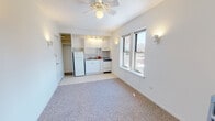 Located on N Winthrop Ave in Chicago's Edgewater neighborhood (60660), this single-floor studio offers a thoughtfully arranged open layout that combines living and kitchen functions efficiently. The main living area features neutral carpet flooring, crisp white walls, and a ceiling fan with integrated lighting, creating a clean and airy atmosphere. Natural light filters in through double-hung windows that frame views of the surrounding cityscape.

The kitchenette is neatly integrated along one wall and is outfitted with white cabinetry — both upper and lower — a gas range, full-size refrigerator, and a single-basin sink with tiled backsplash. Track lighting overhead ensures the cooking area is well-illuminated. An open closet adjacent to the kitchen provides additional storage.

A separate alcove area features a classic cast-iron radiator, offering classic, radiant heating, along with access to a dedicated closet with shelving — ideal for use as a sleeping area.

The bathroom is well-appointed with hex-tile flooring, a full tub and shower with white subway tile surround, a pedestal-style vanity with mirror, built-in open shelving for storage, and a window allowing natural light and ventilation. The overall palette throughout the unit is light and neutral, lending the space a clean, functional character well-suited to urban living.
