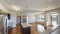 This well-appointed single-floor residence offers a thoughtfully designed open-concept layout that seamlessly connects the kitchen, dining, and living areas. Rich hardwood flooring flows throughout the main living spaces, complemented by neutral-toned walls that create a bright, welcoming atmosphere. The kitchen is a standout feature, showcasing dark espresso cabinetry, granite countertops, and a full suite of stainless steel appliances including a refrigerator, electric range, microwave, and dishwasher. A built-in wine rack adds a distinctive touch, while pendant lighting over the central island provides both task illumination and visual appeal. The spacious living area benefits from multiple windows fitted with horizontal blinds, allowing ample natural light to fill the room, and is finished with a ceiling fan for added comfort. An elegant arched doorway connects the living space to additional rooms, adding architectural character. The bathroom features consistent granite countertops, a full soaking tub with shower, and chrome fixtures that tie the design together cohesively. Additional interior doors lead to private spaces, completing this functional and stylish single-floor layout.