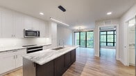 Located in the heart of Royal Oak, Michigan, this thoughtfully designed one-bedroom, one-bathroom residence offers a contemporary living experience with high-end finishes throughout. The open-concept floor plan seamlessly connects the kitchen, dining, and living areas, creating a bright and cohesive space bathed in natural light.

The kitchen is a true centerpiece, showcasing a striking dark-base island topped with veined granite countertops, white shaker cabinetry extending to the ceiling, a sleek subway tile backsplash, and a full suite of stainless steel appliances. A modern linear pendant light above the island adds a refined, industrial-chic touch.

The living area flows effortlessly toward floor-to-ceiling black-framed sliding glass doors that open to a private balcony overlooking lush greenery, complemented by an elegant sputnik chandelier that anchors the space.

The bedroom features a large black-framed grid window that floods the room with natural light and tree-lined views, along with a ceiling fan for year-round comfort.

The bathroom is finished with a granite-topped vanity, white cabinetry, and a tub-shower combo adorned with marble-style tile surround. Light wood-tone luxury vinyl flooring runs throughout, tying the entire residence together with warmth and modern consistency.