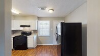 This single-story residence in Memphis, Tennessee offers a practical and well-organized layout across two bedrooms and one bathroom. The interior is finished with neutral gray walls and textured ceilings throughout, creating a consistent and understated aesthetic.

The living area features rich, dark wood-look flooring that extends through the main living spaces, providing a warm and cohesive foundation. A window at the front of the unit allows natural light to filter through, brightening the open connection between the living area and kitchen.

The kitchen is equipped with white cabinetry, light granite-style countertops, and a subway tile backsplash. Black appliances, including a gas range and a large refrigerator, add contrast to the space. A window above the counter and a secondary door provide additional natural light and direct exterior access.

Both bedrooms are carpeted and finished with the same neutral gray walls and textured ceilings. Each room includes at least one window for natural light, and the larger bedroom features two closets, offering generous storage capacity.

The bathroom includes wood-look flooring, a white vanity, and a full tub-shower combination with bold gray brick-style tile surround, adding a distinct design element to the space.
