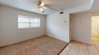 Located at 13214 Bunn Cir in Tampa, Florida, this single-story home offers a straightforward and functional layout designed for comfortable everyday living. The interior is finished with a combination of light tile flooring in the entry and kitchen areas, transitioning to warm, neutral-toned carpet throughout the main living and bedroom spaces. Textured ceilings are featured throughout the home, complemented by ceiling fans with integrated light kits that provide both air circulation and ambient lighting in multiple rooms. Each room benefits from natural light admitted through windows fitted with horizontal blinds, contributing to a bright and airy atmosphere. The rooms are clean and neutrally painted in crisp white, offering a blank canvas for personalization. A closet with louvered doors provides built-in storage in one of the rooms, and a thermostat is conveniently located for climate control. The kitchen is equipped with warm-toned wood cabinetry offering generous upper and lower storage, a coil-top electric range, a full-size refrigerator, and a single-basin sink with a window above — all set on tile flooring. The dollhouse view reveals a compact, well-organized floor plan that includes a bathroom area undergoing updates. Overall, the home presents a functional and adaptable living environment in Tampa.