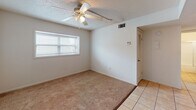 Located at 13214 Bunn Cir in Tampa, Florida, this single-story home offers a straightforward and functional layout designed for comfortable everyday living. The interior is finished with a combination of light tile flooring in the entry and kitchen areas, transitioning to warm, neutral-toned carpet throughout the main living and bedroom spaces. Textured ceilings are featured throughout the home, complemented by ceiling fans with integrated light kits that provide both air circulation and ambient lighting in multiple rooms. Each room benefits from natural light admitted through windows fitted with horizontal blinds, contributing to a bright and airy atmosphere. The rooms are clean and neutrally painted in crisp white, offering a blank canvas for personalization. A closet with louvered doors provides built-in storage in one of the rooms, and a thermostat is conveniently located for climate control. The kitchen is equipped with warm-toned wood cabinetry offering generous upper and lower storage, a coil-top electric range, a full-size refrigerator, and a single-basin sink with a window above — all set on tile flooring. The dollhouse view reveals a compact, well-organized floor plan that includes a bathroom area undergoing updates. Overall, the home presents a functional and adaptable living environment in Tampa.