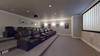 Located at 121 Towne St in Stamford, Connecticut, this dedicated private home theater delivers a true cinema experience within a thoughtfully designed single-level space. The room is arranged with multiple rows of plush, dark leather recliner seats positioned on a raised tiered platform, ensuring unobstructed sightlines to the large front projection screen from every seat. Each recliner features built-in cup holders, adding a practical touch that mirrors a commercial movie theater setting. A ceiling-mounted projector anchors the audio-visual setup, projecting onto a wide, centrally positioned screen that dominates the front wall. The walls are finished in a neutral gray tone and adorned with a curated collection of framed classic movie posters — including iconic titles such as Jaws, E.T., Vertigo, Breakfast at Tiffany's, and The Godfather — creating an engaging cinematic atmosphere. Recessed ceiling lighting and wall sconces provide warm, adjustable ambient illumination throughout the room. Crown molding runs along the ceiling perimeter, lending a polished, finished look to the space. Wall-to-wall carpet in a complementary gray tone enhances acoustics while adding comfort underfoot. Two access doors provide convenient entry and exit points, and the overall layout is optimized for an immersive, distraction-free viewing environment.