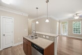 This single-story residence spans 1,170 square feet and features 3 bedrooms, 2 bathrooms, a combined kitchen and living area, a dedicated laundry room, two hallways, and a closet. The open-concept kitchen and living room serves as the heart of the home, anchored by a central island with a granite countertop, undermount sink, and pendant lighting. Rich wood cabinetry pairs with stainless steel appliances, while light hardwood-style flooring and crown molding throughout add a polished finish. The living area benefits from natural light and ceiling fans for year-round comfort. The primary bedroom measures 170 square feet and features plush carpet, a ceiling fan, and access to a walk-in closet equipped with wire shelving. The two additional bedrooms also feature carpet flooring and large windows with outdoor views. Both bathrooms are finished with granite-topped wood vanities and hardwood-style flooring; one includes a soaking tub with shower combo. The dedicated laundry room accommodates a full-size washer and dryer and includes upper cabinetry and a storage shelf. Neutral warm-toned walls, consistent trim work, and cohesive finishes create a clean, functional living environment throughout.