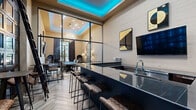 Located at 3800 SW Richsmith Rd in Bentonville, Arkansas, this upscale clubhouse facility offers an impressive array of amenities across a single, expansive floor. The grand entrance lobby sets an elegant tone with polished marble-style tile flooring, coffered ceilings accented by vibrant teal ambient lighting, structural columns, wall sconces, and curated abstract artwork. A linear fireplace and plush seating arrangements create an inviting yet sophisticated atmosphere.

The entertainment lounge features soft teal walls, bold patterned carpeting, and elegant chandelier lighting. Pool tables, high-top bar tables, large-screen televisions, and direct access to an outdoor patio make this a versatile social hub. Adjacent to the lounge is a sleek bar area outfitted with dark granite countertops, bar seating, a wet bar with sink, and floor-to-ceiling glass partitions that connect to the gaming space beyond.

A dedicated private theater room impresses with rows of red upholstered cinema-style seating, dramatic floor-to-ceiling red drapery, wall sconces, and a projector system — ideal for private screenings. The business center provides a quiet workspace with a large live-edge wood conference table, high ceilings, and natural light from expansive windows. A cozy reading nook with tall ceilings and artistic wall displays rounds out this thoughtfully designed facility.