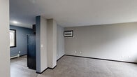 Located at 5150 16th Ave SW in Cedar Rapids, Iowa, this single-floor unit offers a practical and well-organized layout designed for comfortable everyday living. The kitchen is a standout feature, equipped with rich dark wood cabinetry offering ample storage, stone-look countertops, black appliances including a range, dishwasher, and built-in microwave, and a double-basin sink — all set against cool blue walls and durable wood-look flooring. The living area provides a generous open feel, featuring neutral gray walls, plush carpeting, and a wall-mounted air conditioning unit for climate control. Multiple bedrooms carry a consistent design language throughout, with warm beige tones, soft carpeting, ceiling fans, and baseboard heating units positioned beneath large windows with dark frames. These windows invite natural light and offer views of the surrounding neighborhood and greenery. The bathroom includes a tub and shower combination enclosed by sliding frosted glass doors, paired with blue-toned walls that add a subtle pop of color. Overall, the space presents a clean, functional interior with consistent finishes and practical amenities suited for residential use.