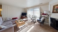 This single-floor residence offers a thoughtfully arranged layout that balances comfort and functionality across its key living spaces. The main living area features plush carpeting, a classic fireplace with a white mantel, and a welcoming entryway, with natural light filtering in to create a warm and inviting atmosphere. An adjacent section of the living space is enhanced by vertical shiplap-style wall paneling and a large sliding glass door with sheer curtains, allowing abundant sunlight and providing access to an outdoor area.

The kitchen is designed with practicality in mind, featuring white cabinetry, a peninsula countertop with light wood-tone flooring, and essential appliances including a range and refrigerator. The layout encourages easy movement between cooking and dining areas.

The residence includes two bedrooms, both finished with soft carpeting and neutral wall tones. The primary bedroom features the same shiplap-style accent wall and a walk-in closet, while the second bedroom offers a windowed wall and its own closet access, providing ample storage. The full bathroom is appointed with warm tile flooring, a soaking tub, a large wall mirror, and a white vanity with generous cabinet space beneath. Together, these spaces create a cohesive and comfortable living environment.