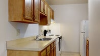 This single-floor residence offers a practical and well-organized layout across several distinct rooms. The galley-style kitchen is efficiently arranged, featuring warm oak cabinetry with ample upper and lower storage, light-toned laminate countertops, a stainless steel sink, and white appliances including an electric range and refrigerator. Tile flooring completes the kitchen's clean, functional aesthetic.

The living area is carpeted and generously proportioned, with neutral beige walls that create a bright, understated atmosphere. A large sliding glass door opens to a private balcony, framing views of mature trees and surrounding greenery, and allowing natural light to fill the space. Panel curtains accompany the sliding door, offering light control and privacy.

Multiple bedrooms are present, each carpeted and finished with neutral walls. Each bedroom includes a built-in closet with shelving and hanging rods, providing organized storage. Windows in the bedrooms allow natural light to enter, with some offering additional outdoor views.

The bathroom features tile flooring, a vanity with oak cabinetry, a white countertop, and a mirrored medicine cabinet. A separate water closet includes a tub and white tile surround. Throughout the unit, the overall ambiance is clean, neutral, and move-in ready.