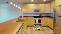 This single-floor residence offers a thoughtfully designed layout with a cohesive blend of functional and comfortable living spaces. The kitchen is a standout feature, equipped with light maple cabinetry, warm brown countertops, stainless steel appliances including a gas range, microwave, and refrigerator, and a double stainless steel sink. A peninsula with pendant track lighting separates the kitchen from the open living area, which features rich hardwood flooring, recessed lighting, and a sliding glass door that opens to an outdoor balcony, allowing natural light to fill the space.

The bedrooms are carpeted for comfort, each featuring neutral tones, standard windows with blinds, and ceiling fixtures. One bedroom includes a ceiling fan and a window with views of surrounding greenery. The hallway connecting the rooms is carpeted and leads to the bathrooms and additional spaces.

Two bathrooms serve the residence. One features a long vanity with light maple cabinetry, a warm countertop, tile flooring, and a large mirror. The second bathroom includes a tub-shower combination, a wall-mounted vanity with storage, and round mirrors. A dedicated laundry room houses a full-size washer and dryer alongside additional cabinetry for storage.