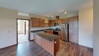 This thoughtfully designed single-floor residence blends modern finishes with a comfortable, functional layout. The kitchen serves as a standout feature, showcasing rich wood cabinetry, dark granite countertops, a peninsula for additional prep and seating space, and a full suite of stainless steel appliances including a refrigerator, range, microwave, and dishwasher. Track lighting illuminates the space, while durable hardwood-style flooring ties the kitchen and living areas together seamlessly.

The living area extends from the kitchen and opens toward a balcony through a glass door, allowing an abundance of natural light to fill the space. Exposed ductwork adds an industrial loft-inspired character, complementing the soaring ceiling height in this area.

The bedrooms are carpeted and generously sized, each benefiting from multiple windows that frame lush greenery outdoors. One bedroom features particularly elevated ceilings and a tray ceiling detail, enhancing the sense of spaciousness.

Both bathrooms mirror the kitchen's refined aesthetic with dark granite vanity countertops, warm wood cabinetry, and hardwood-style flooring. One bathroom includes a tub-shower combination, while the other offers a separate shower. In-unit laundry is also conveniently accessible within the layout.