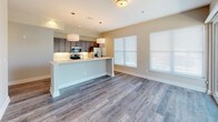 This single-floor unit offers a thoughtfully designed open-concept layout with contemporary finishes throughout. The kitchen serves as a central highlight, featuring gray shaker-style cabinetry extending to the ceiling, a full suite of stainless steel appliances including a French door refrigerator, electric range, and built-in microwave. A quartz-topped island provides additional workspace and casual seating, while wood-look plank flooring adds warmth and durability underfoot.

The living area extends naturally from the kitchen, benefiting from wood-look flooring and a sliding glass door that invites natural light and outdoor access. A secondary window further brightens the space. The bedrooms are finished with plush neutral carpeting and feature ceiling fans for comfort. One bedroom includes a walk-in closet, offering practical storage. A ceiling fan with a light fixture is also present.

The bathroom is finished with large-format tile flooring, a wide vanity with white quartz countertops, dual sinks, and brushed nickel hardware, accompanied by a well-sized mirror. Neutral warm-toned walls are consistent throughout the unit, contributing to a cohesive and inviting aesthetic overall.