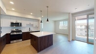 Located at 1625 Santa Venetia St in Chula Vista, California, this single-floor residence showcases a clean, contemporary design with consistent modern finishes throughout. The heart of the home is a well-appointed kitchen featuring a striking two-tone cabinetry scheme — rich dark wood lower cabinets paired with crisp white upper cabinets — complemented by a white quartz countertop island with pendant lighting overhead. Stainless steel appliances, including a French door refrigerator, gas range, and microwave, complete the functional and stylish culinary space. Light wood-style flooring flows seamlessly from the kitchen into the open living area, which benefits from natural light through window blinds. The bedrooms offer a comfortable retreat; select rooms feature plush carpet flooring, ceiling fans, and generous windows that invite natural light and outdoor views, with at least one bedroom providing direct access to a private balcony. The bathroom is finished with a dark wood vanity, white quartz countertop, a large framed mirror, open shelving, and light wood-style flooring, maintaining the cohesive modern aesthetic found throughout the home. Overall, the space presents a bright, neutral palette ideal for contemporary living.
