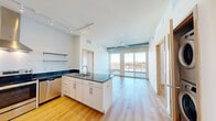 Located at 2905 Harriet Ave in Minneapolis, MN, this 2-bedroom, 2-bathroom unit offers a thoughtfully designed open-concept layout with light hardwood flooring throughout. The kitchen is a standout feature, showcasing white cabinetry, dark stone countertops, a central island with a built-in sink, stainless steel appliances including a refrigerator and range with a sleek hood vent, and track lighting overhead. Open to the kitchen, the living area is bright and airy, benefiting from large sliding glass doors that lead to a private balcony and offer sweeping views of the Minneapolis skyline. Exposed metallic ductwork adds an industrial-modern accent carried through the bedrooms. Both bedrooms are well-lit with large windows and sliding glass doors opening to outdoor balcony spaces, framing impressive city and neighborhood views. The two bathrooms are finished with tile flooring, white vanities topped with dark counters, and full tub-shower combinations. Clean lines, neutral tones, and abundant natural light define the overall aesthetic, creating a contemporary and functional living environment in the heart of Minneapolis.