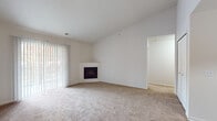 This single-story residence offers a clean, neutral palette throughout, designed to maximize comfort and functionality. The entry opens into a generously sized living area featuring vaulted ceilings that lend an airy, open feel. Warm hardwood-style flooring in the entryway transitions to plush carpeting in the main living space, which is anchored by a corner fireplace and a large sliding door with vertical blinds that invites natural light and outdoor views.

The kitchen is efficiently laid out in a galley style and opens to the living area via a breakfast bar peninsula. Light wood cabinetry, laminate countertops, a double-basin sink, and white appliances including a range and refrigerator equip the space well. A dedicated laundry room directly off the kitchen houses a full-size washer and dryer, adding everyday convenience.

The bedrooms are carpeted and bright, each featuring vaulted or elevated ceilings and large windows dressed with vertical blinds. The bathrooms are finished with light wood vanities, oval sinks, and hardwood-style flooring, maintaining a consistent, cohesive aesthetic throughout the home. Overall, the space presents a functional and comfortable layout with a light, understated design.