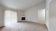 This single-story residence offers a clean, neutral palette throughout, designed to maximize comfort and functionality. The entry opens into a generously sized living area featuring vaulted ceilings that lend an airy, open feel. Warm hardwood-style flooring in the entryway transitions to plush carpeting in the main living space, which is anchored by a corner fireplace and a large sliding door with vertical blinds that invites natural light and outdoor views.

The kitchen is efficiently laid out in a galley style and opens to the living area via a breakfast bar peninsula. Light wood cabinetry, laminate countertops, a double-basin sink, and white appliances including a range and refrigerator equip the space well. A dedicated laundry room directly off the kitchen houses a full-size washer and dryer, adding everyday convenience.

The bedrooms are carpeted and bright, each featuring vaulted or elevated ceilings and large windows dressed with vertical blinds. The bathrooms are finished with light wood vanities, oval sinks, and hardwood-style flooring, maintaining a consistent, cohesive aesthetic throughout the home. Overall, the space presents a functional and comfortable layout with a light, understated design.