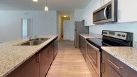 This single-story residence is designed with a clean, modern aesthetic and a thoughtfully open layout. The main living area features wood-look flooring and a ceiling fan overhead, flowing seamlessly into the kitchen, which serves as a functional centerpiece of the space. The kitchen is outfitted with stainless steel appliances, including a refrigerator, electric range, and over-the-range microwave. Dark lower cabinetry contrasts with white upper cabinets, while granite-style countertops and pendant lighting add a polished finish. A kitchen island with an undermount sink provides additional prep and casual dining space.

The bedrooms are finished with plush carpeting, ceiling fans, and windows fitted with blinds that allow natural light while maintaining privacy. Each room offers a comfortable sense of scale with neutral white walls and clean trim throughout.

The bathrooms are finished with light wood-look flooring, wood-toned vanity cabinetry topped with granite-style counters, and a full tub-shower combination with white tile surround. The overall ambiance of the residence is bright, neutral, and move-in ready, with consistent finishes that create a cohesive and welcoming atmosphere.