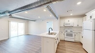 Located at 1542 Michigan St NE in Grand Rapids, Michigan, this thoughtfully designed single-floor unit blends modern industrial aesthetics with clean, contemporary finishes. The open-concept living and kitchen area serves as the heart of the space, where exposed metallic ductwork adds an industrial character to the bright, white interior. The kitchen is well-appointed with white shaker cabinetry featuring matte black hardware, a subway tile backsplash, a central island with a marble-look countertop and double-basin sink, and full appliances including a refrigerator, range, and over-the-range microwave. The living area extends to a sliding glass door that opens to a private balcony, allowing natural light to fill the space. Luxury vinyl plank flooring runs throughout the main living areas, complementing the clean, neutral color palette. The bedrooms are carpeted for comfort and include windows with blinds that invite natural light. The bathroom features a walk-in shower, white vanity cabinetry with matte black hardware, and an adjacent walk-in closet with wire shelving. A secondary bathroom includes a toilet and hardwood-style flooring. The overall ambiance is bright, airy, and move-in ready.