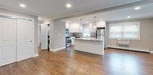 This single-floor residence offers a thoughtfully designed open-concept layout that seamlessly connects the living, dining, and kitchen areas. Rich hardwood flooring flows throughout the main living spaces, complemented by neutral taupe walls and crisp crown molding that lend an air of refined elegance. Recessed lighting and pendant fixtures provide ample illumination throughout.

The kitchen is a standout feature, boasting white shaker-style cabinetry extending to the ceiling, granite countertops, a generous center island with seating, and a full suite of stainless steel appliances including a gas range, microwave, dishwasher, and refrigerator. Natural light pours in through multiple windows fitted with blinds.

The spacious bedroom features hardwood floors, crown molding, a ceiling fan, and a large window overlooking lush greenery. It is complemented by an expansive walk-in closet outfitted with a comprehensive built-in shelving and hanging system, offering exceptional storage capacity.

Two updated bathrooms serve the space. The full bathroom includes a soaking tub with shower, a mosaic tile accent border, travertine-style tile flooring, a dark espresso vanity with a light countertop, and a mirrored medicine cabinet. A second bathroom features a glass-door shower, matching vanity, and mirrored cabinet. An in-unit laundry area is also conveniently accessible off the main living space.