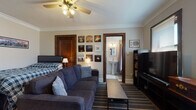 Located at 833 N 15th St in Milwaukee, Wisconsin, this single-floor unit showcases classic architectural character throughout, highlighted by crown molding, dark wood door trim, and a ceiling fan with a brass fixture in the main living area. The combined living and sleeping space is thoughtfully arranged, accommodating a full-size bed alongside a comfortable sectional sofa and a coffee table, creating a versatile, multi-use room. A gallery wall of framed artwork adds a personalized, curated touch, while a bookcase and entertainment center offer functional storage and media options. The adjacent living room extension features terrazzo flooring, two windows with blinds that allow natural light, and a vintage cast-iron radiator that speaks to the building's historic character. The galley-style kitchen is equipped with dark wood cabinetry, a gas range, a refrigerator, and granite-look countertops, providing efficient use of space for meal preparation. The full bathroom is finished with classic penny-tile flooring, a pedestal sink, a tiled soaking tub with a shower, and a glass block window that brings in soft, diffused natural light. A walk-in closet area provides generous storage. Overall, the space blends historic Milwaukee charm with practical, functional living.