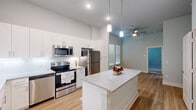 Located at 1619 N Frazier Street in Conroe, TX, this well-appointed one-bedroom, one-bathroom unit offers a thoughtfully designed layout that maximizes its compact footprint. The open-concept kitchen serves as the heart of the home, showcasing crisp white shaker cabinetry extending to the ceiling, a granite-topped center island with pendant lighting overhead, and a full suite of stainless steel appliances including a refrigerator, electric range, microwave, and dishwasher. Light wood-look flooring runs throughout the main living areas, complemented by elevated ceilings that lend an airy, spacious feel. A ceiling fan in the living area adds both function and comfort. The bedroom features soft carpeting, soothing sage-green walls, and dual windows fitted with blinds that allow for natural light control. A dedicated walk-in closet provides double-rod hanging storage and built-in shelving, offering generous organizational capacity. The bathroom is finished with a white vanity, granite countertop, a large mirror, open shelving, and wood-look flooring that ties cohesively to the rest of the unit. The overall design palette of soft grays, whites, and warm wood tones creates a clean, modern, and inviting atmosphere throughout.