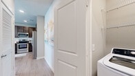 This well-designed single-floor residence offers a thoughtfully planned layout that balances functionality with modern style. The open-concept kitchen and living area serves as the heart of the home, featuring rich dark-brown cabinetry, stainless steel appliances, a subway tile backsplash, and a granite-topped center island with bar seating — ideal for casual dining or entertaining. Light wood-style flooring flows seamlessly throughout, enhancing the bright, airy atmosphere created by an abundance of natural light streaming through large windows dressed with sheer curtains and blinds.

The living area is generously proportioned, with a ceiling fan overhead and multiple windows that invite natural light from multiple directions, creating a warm and welcoming environment. The bedroom continues this comfortable aesthetic, featuring its own ceiling fan, a large window with outdoor views, and ample space for full-sized furniture.

The full bathroom is finished with matching granite countertops, a dark-cabinetry vanity with a brushed nickel faucet, a large mirror, and a shower-tub combination. A walk-in closet with built-in wire shelving is conveniently accessible from the bathroom. Completing the unit is a dedicated in-unit laundry room equipped with a full-sized washer and dryer, adding everyday practicality to this modern residence.