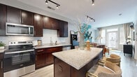 Located at 5720 Fishers Lane in Rockville, MD, this thoughtfully designed one-bedroom, one-bathroom residence offers an efficient and stylish single-floor layout. The open-concept kitchen and living area form the heart of the home, where rich dark-wood cabinetry, granite countertops, a subway tile backsplash, and stainless steel appliances define a contemporary kitchen anchored by a central island with bar seating. Light hardwood-style flooring flows throughout the main living areas, enhancing the sense of openness. The living room is bright and inviting, featuring large windows and a glass door that opens to a private balcony, flooding the space with natural light. A bold teal accent wall with mounted botanical décor adds a distinctive, lively character to the room. The bedroom offers plush carpeting, generous natural light from dual windows, and a striking geometric orange accent wall that gives the room a bold, modern feel. The full bathroom is finished with tile flooring, a granite-topped vanity with dark cabinetry, and a classic subway-tiled tub-shower combination. Throughout the residence, a cohesive palette of modern finishes and vibrant design accents creates a dynamic yet comfortable living environment.