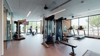 This fitness center in Vancouver, Washington is designed with a clean, contemporary aesthetic that prioritizes both functionality and comfort. The single-level space features a bright, open layout illuminated by a combination of recessed linear lighting and an abundance of natural light streaming through expansive floor-to-ceiling windows along the exterior walls. These large glass panels provide unobstructed outdoor views, creating an airy atmosphere that enhances the workout experience.

The flooring throughout transitions between textured rubber and hard surfaces, offering appropriate support across different workout zones. A multi-station cable strength machine serves as a central fixture, accompanied by a dedicated weight bench. The cardio section is well-equipped with treadmills and elliptical trainers, each positioned to take advantage of the outdoor views. Wall-mounted televisions are strategically placed throughout the space for entertainment during workouts.

A smart mirror fitness display is mounted on one wall, while a free weight rack offers additional strength training options. Ceiling fans provide supplemental air circulation alongside the HVAC system. Motivational wall typography reading "Be Stronger Than Your Excuses" adds an energetic character to the space. Textured concrete columns contribute an architectural contrast to the otherwise modern, minimalist design.