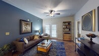 This thoughtfully designed single-floor residence makes a strong visual impression through a cohesive blue-toned color palette carried throughout its principal rooms. The living area anchors the home with rich hardwood flooring, a bold slate-blue accent wall, a ceiling fan, and French doors that invite natural light and provide access to the outdoors. A dedicated dining area off the main living space features tile flooring, an elegant chandelier, and ample room for entertaining. The kitchen is well-equipped with warm wood cabinetry, granite-look countertops, stainless steel appliances, and hardwood-style flooring that ties the space together seamlessly. A connecting hallway with character-rich hardwood floors leads to the private quarters, passing a bathroom that features a vanity with stone-look countertops and a full tub-shower combination. The bedrooms are generously sized, each featuring plush carpeting, ceiling fans, and striking deep navy accent walls that create a calm and restful atmosphere. Multiple windows dressed with blinds and curtains allow for controlled natural light. Throughout the home, consistent design choices — from the accent wall colors to the warm wood tones — create a unified and inviting ambiance suited for comfortable everyday living.
