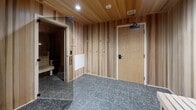 Located in Duluth, Minnesota, this thoughtfully designed wellness suite offers a refined sauna and bathing experience within a compact, single-floor layout. The space is unified by a warm material palette of natural wood paneling — light cedar in the hallway and changing area, transitioning to rich, deep-toned cedar within the sauna room itself — creating a cohesive and calming atmosphere throughout.

The sauna room is the centerpiece of the suite, finished entirely in aromatic cedar on the walls, ceiling, and tiered benches. Subtle LED strip lighting runs along the upper bench level, casting a warm ambient glow that enhances the intimate, restorative atmosphere. The floor features dark penny-round pebble tile, adding both texture and contrast to the warm wood tones.

Adjacent to the sauna, a dedicated shower area is finished with deep charcoal square tile on the walls and the same pebble tile flooring, equipped with a shower base and curtain for privacy. A glass door connects the wet and dry areas seamlessly.

The hallway and changing area are lined with vertical light cedar wood paneling and feature a simple wooden bench for convenience, recessed ceiling lighting, and a pebble tile floor that continues the spa-like aesthetic. A solid wood entry door with black hardware completes the suite's polished, modern design.