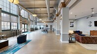 Located in Hartford, CT, this expansive single-floor space blends industrial-loft character with modern amenities across a generous footprint. Soaring double-height ceilings, exposed silver ductwork, and warm wood beam accents define the architectural identity throughout. Floor-to-ceiling multi-pane windows flood the interiors with abundant natural light and offer open views of the surrounding urban streetscape.

The main living area is anchored by tufted leather sofas, a rustic wood coffee table, and a vibrant blue area rug, creating a welcoming lounge atmosphere. Adjacent, a well-appointed kitchen features dark wood cabinetry, granite countertops, stainless steel appliances, and pendant lighting above a central workspace — ideal for entertaining or communal gatherings. Bar-height seating and high-top tables are strategically placed near the towering windows, encouraging social interaction.

A dedicated game room offers a full-size billiard table with a vivid red felt surface, a ping-pong table, wall-mounted television, and pendant lighting — all set beneath dramatically tall ceilings. The office area provides a quieter retreat, with curated wall art and flexible seating. Polished concrete flooring flows seamlessly throughout, tying together each zone. The overall ambiance is modern and dynamic, with an industrial aesthetic softened by thoughtful furnishings.