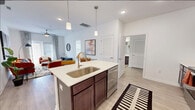 This single-floor residence at Amherst Villa Court in Charlotte, NC, offers a well-designed open-concept layout that seamlessly connects the kitchen, dining, and living areas. The kitchen serves as a central hub, anchored by a large island with a white quartz countertop, an undermount sink, and elegant pendant lighting overhead. Rich dark-wood cabinetry lines the walls, complemented by a full suite of stainless steel appliances, including a refrigerator with ice maker, range, microwave, and dishwasher. Light wood-style flooring flows throughout the main living areas, enhancing the bright, airy atmosphere created by white walls and recessed lighting.

The living room extends naturally from the kitchen, featuring a ceiling fan, large windows that invite natural light, and ample room for comfortable furnishings. The bedroom is a calm retreat finished with plush carpet, a ceiling fan, and a generous window. It connects to a spacious walk-in closet outfitted with multi-tiered wire shelving for organized storage. The ensuite bathroom features dark cabinetry, a wide vanity with a large mirror, and wood-style flooring, maintaining a consistent, polished aesthetic throughout the residence.