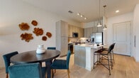 Located at 3017 Clementine Ct in Sarasota, Florida, this modern single-story residence offers a thoughtfully designed open-concept layout that seamlessly connects the kitchen, dining, and living areas. The kitchen is a standout feature, showcasing light wood-grain cabinetry extending to the ceiling, granite countertops, a central island with bar seating, stylish pendant lighting, and a full suite of stainless steel appliances including a French door refrigerator, range, and microwave. Light wood-style flooring flows throughout the main living areas, enhancing the home's bright and airy ambiance. The living room is generously proportioned, bathed in natural light from sliding glass doors that open to an outdoor view of lush greenery and palm trees, complemented by a ceiling fan overhead. The bedrooms are carpeted and serene, with one featuring a bold teal accent wall and another offering soft neutral tones and natural light through large windows with elegant draping. The bathroom is finished with granite countertops, modern flat-front cabinetry, and large-format tile flooring. Throughout the home, clean lines, contemporary finishes, and a cohesive coastal-modern aesthetic create an inviting and functional living environment.