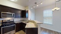 This two-story residence offers a well-appointed layout with a cohesive blend of modern finishes and functional design throughout both levels. The kitchen serves as a central highlight, featuring dark espresso cabinetry, light granite countertops, a peninsula with additional counter space, stainless steel appliances including a gas range, microwave, and refrigerator, and a track lighting system overhead. Hardwood-style flooring runs through the kitchen and adjoining areas, lending warmth to the main living spaces.

A carpeted staircase with a warm wood handrail connects the two floors, with bedrooms found upstairs. The bedrooms are carpeted and bathed in natural light, with one room featuring a ceiling fan and another offering built-in shelving with an arched accent detail and large sliding glass doors dressed in sheer curtains. The bathrooms are finished with matching granite vanity countertops, dark cabinetry, and a full tub-and-shower combination with clean white tile surround. An in-unit laundry area with a side-by-side washer and dryer adds practical convenience to the home's overall offering.
