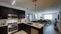 This single-floor space showcases a thoughtfully designed open-concept layout that seamlessly integrates the kitchen and living area. The kitchen is a standout feature, outfitted with bold dark cabinetry that contrasts elegantly against light granite countertops. Stainless steel appliances, including a built-in microwave, gas range, and dishwasher, add a polished, modern touch. A peninsula with an undermount sink serves as both a functional workspace and a natural divider between the kitchen and living area, illuminated by two stylish pendant lights that enhance the contemporary aesthetic.

The living area extends naturally from the kitchen, creating a spacious and cohesive environment ideal for entertaining or relaxing. Track lighting runs along the ceiling, providing flexible ambient illumination throughout. Light hardwood-style flooring runs continuously across both areas, reinforcing the open feel. A large window at the far end of the living space allows natural light to filter in, brightening the interior. The overall design balances clean lines, neutral tones, and modern fixtures to create a refined, functional living environment.